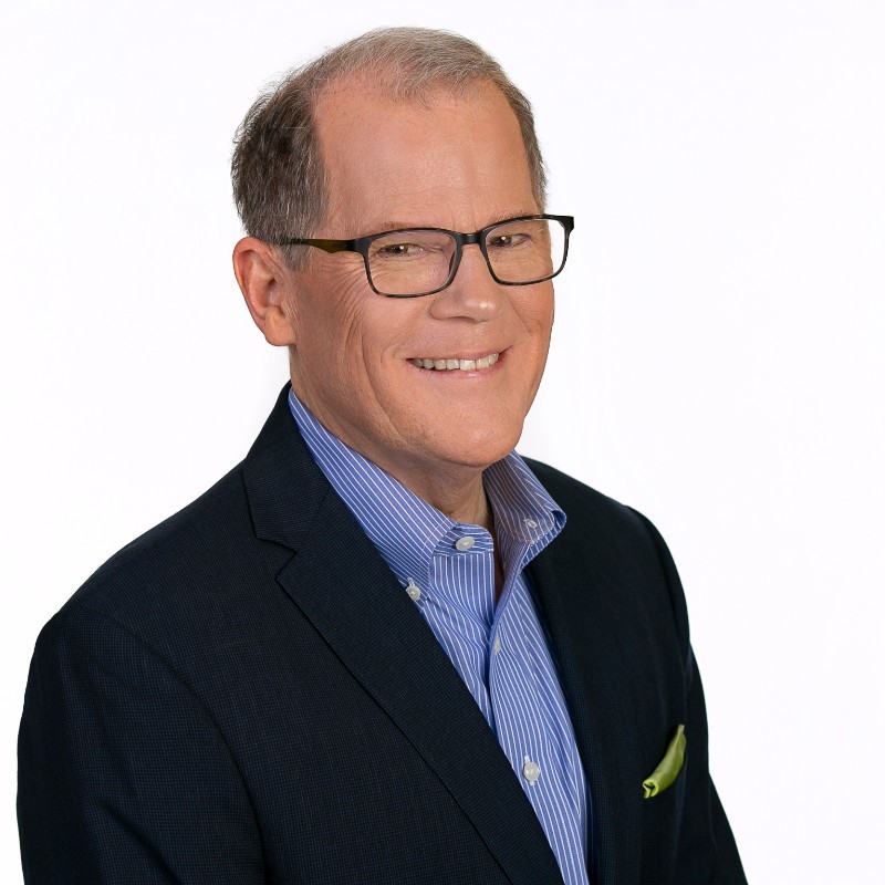 Roger Grannis, Founder and CEO of the Grannis Group, professional profile headshot of his chest and head. He wears a dark jacket, with a light blue button down shirt and a matching pocket  square with glasses and a big smile.